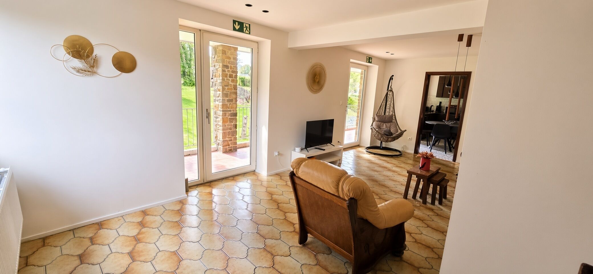 A spacious living area with a stone-tiled floor, a leather sofa, a television, and a dining area with a hanging chair.