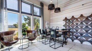 A modern interior with large windows, a geometric wall design, and a metal-framed table with chairs. - BrightHaven Frisco - 1BR+ EV Parking near The Star (Frisco)