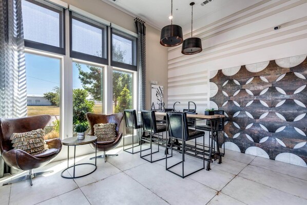 A modern interior with large windows, a geometric wall design, and a metal-framed table with chairs.