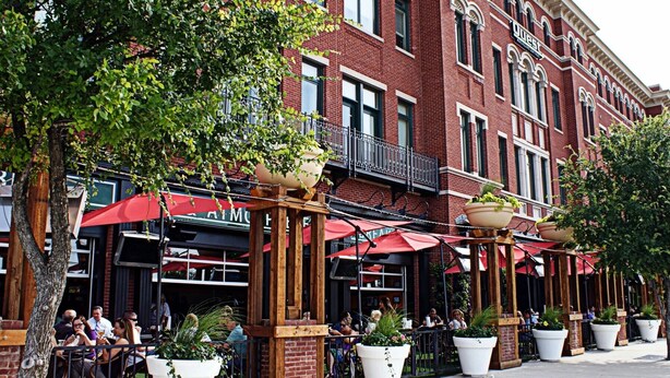 An outdoor cafe with brick buildings, outdoor seating, and potted plants. - BrightHaven Frisco - 1BR+ EV Parking near The Star (Frisco)