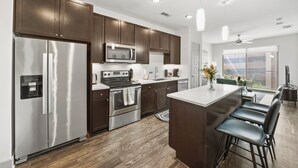 A modern kitchen with stainless steel appliances, dark wooden cabinets, and a central island with bar stools. - BrightHaven Frisco - 1BR+ EV Parking near The Star (Frisco)