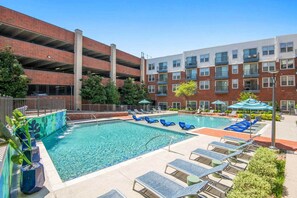 A pool area with lounge chairs and a multi-story building in the background.