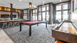 A modern pool table with a red felt surface, a foosball table, and a bar area with stools. - BrightHaven Frisco - 1BR+ EV Parking near The Star (Frisco)