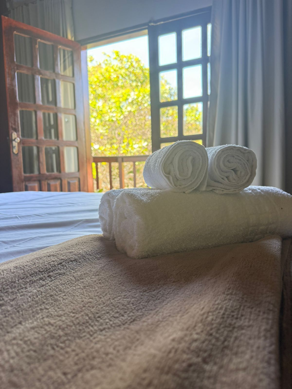 Cama com toalha branca enrolada e manta bege.
