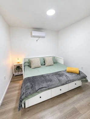 Ein Schlafzimmer mit Bett, Nachttisch, Lampe und Klimaanlage.