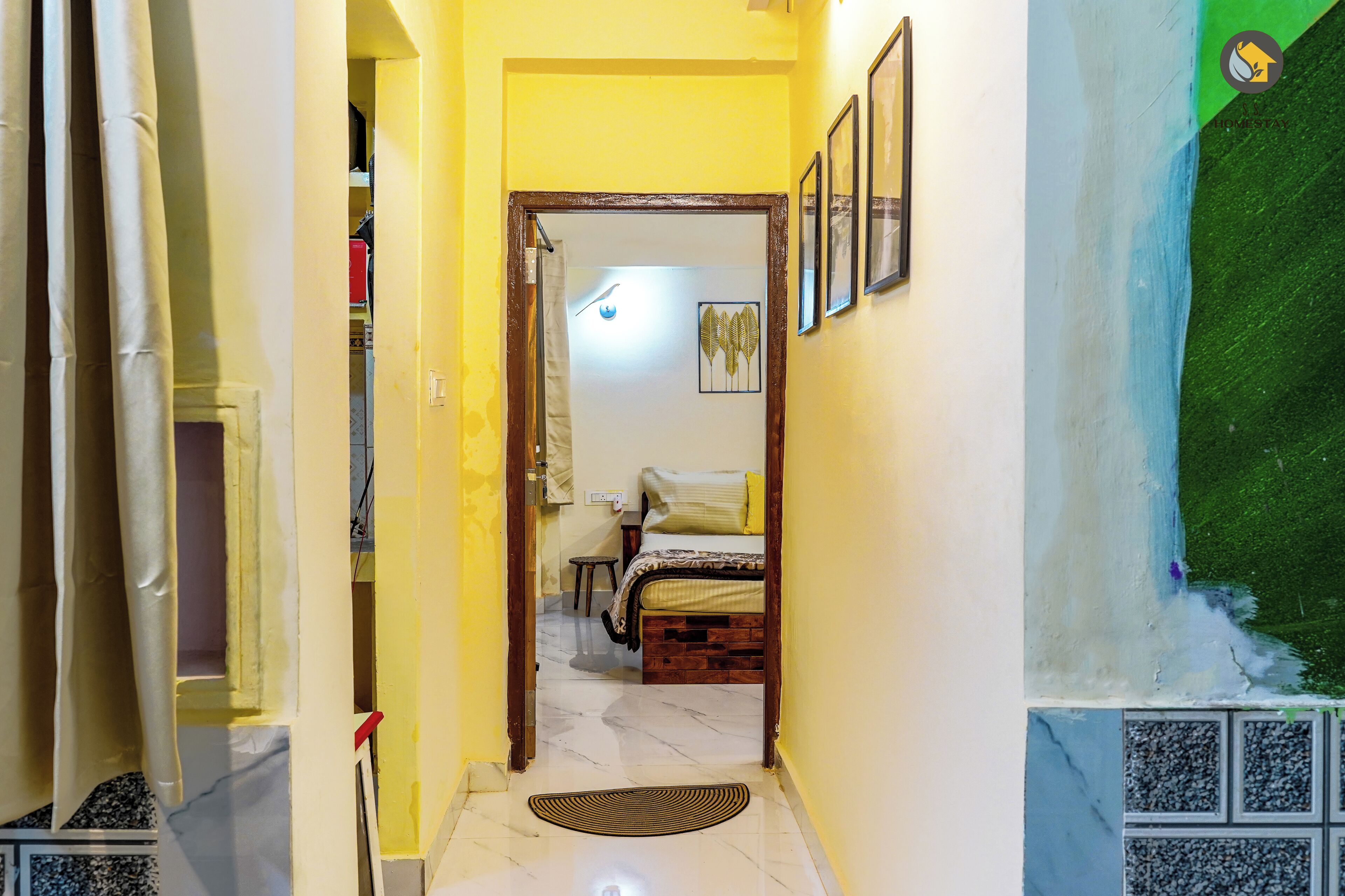 A narrow hallway with a bed at the end, a door on the left, and a wall with framed pictures.