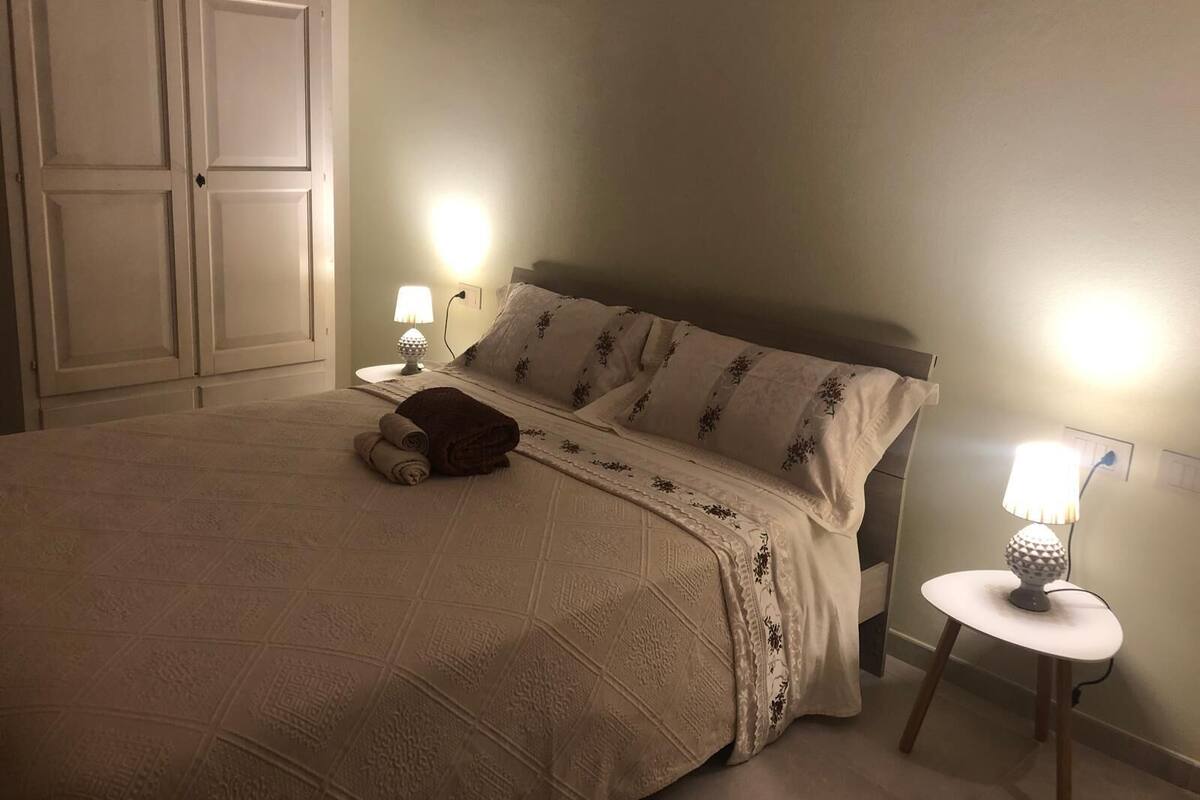 A bedroom with a bed, two bedside lamps, a nightstand, and a wardrobe.