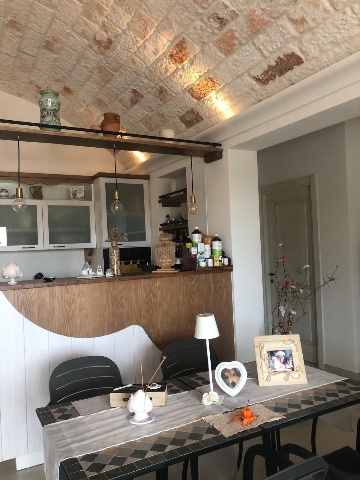 Un comedor con mantel a cuadros, un adorno con forma de corazón blanco, una foto enmarco y un florero con flores.