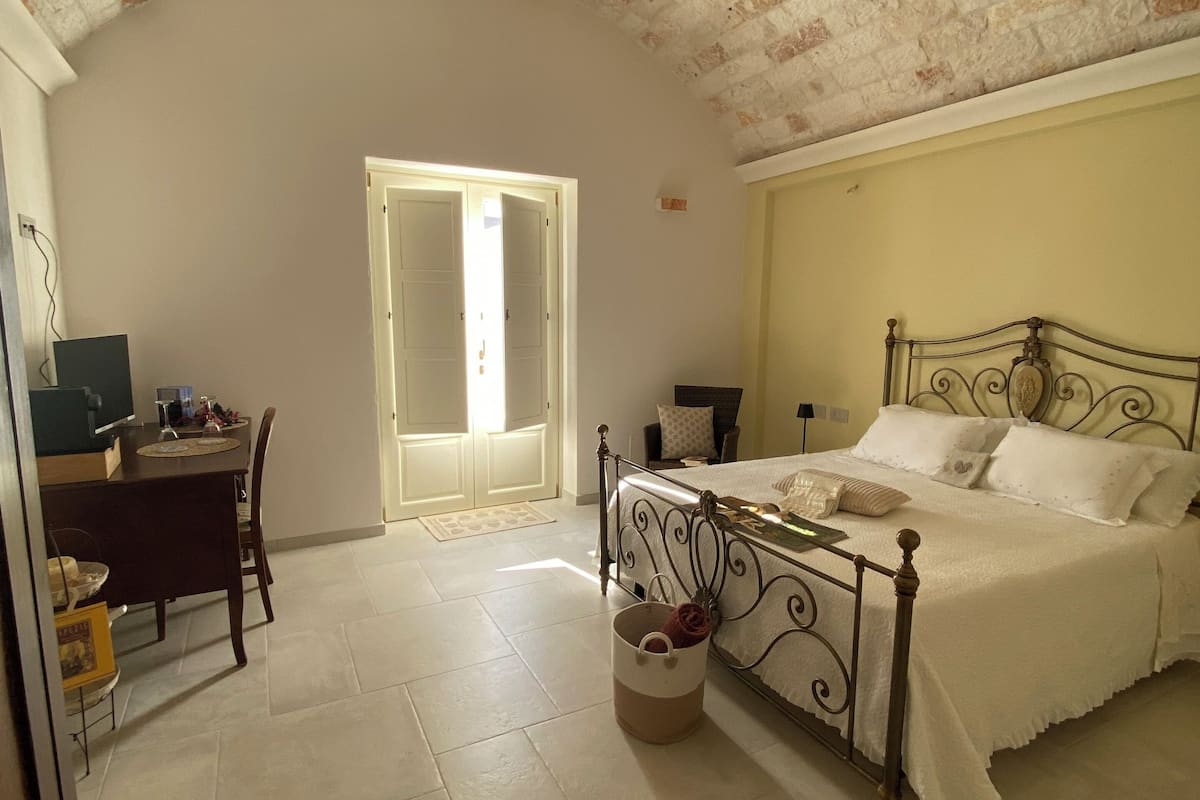 A bedroom with a bed, a desk, and a chair. There is a door leading to another room.