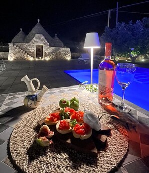 A table set with food and drinks, a lamp, and a stone building in the background. - Villa Itriò  (Martina Franca)