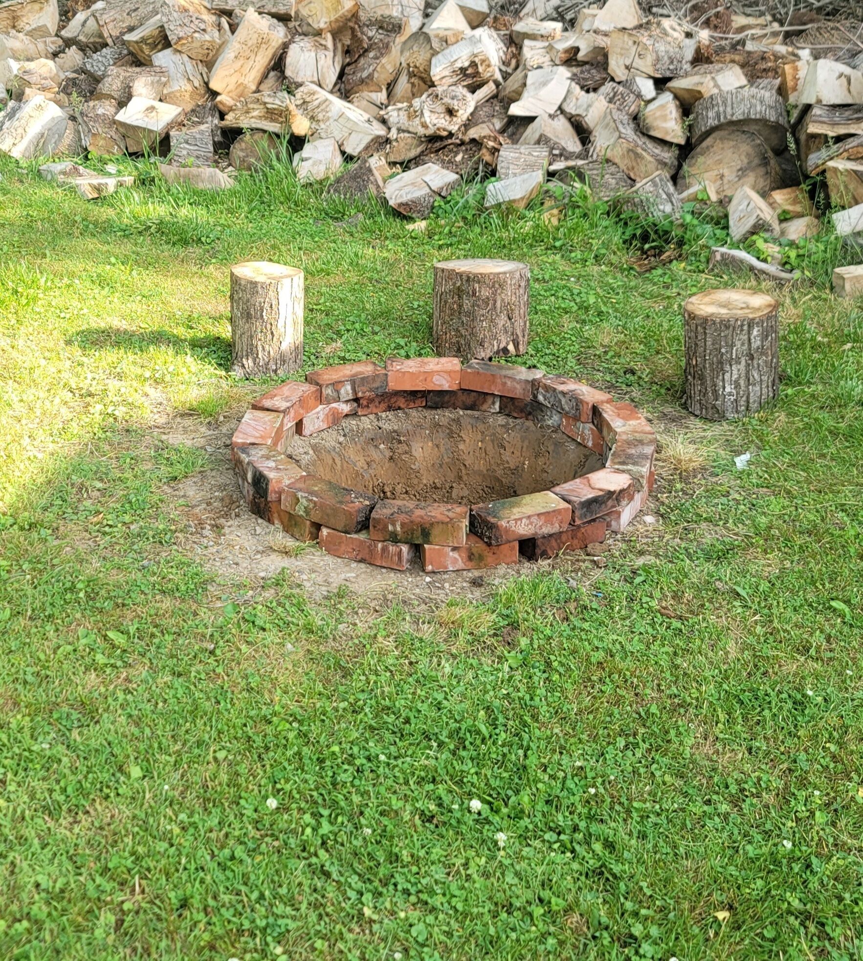 Un hogar circular rodeado de ladrillos, con leña y un montón de astillas al fondo.