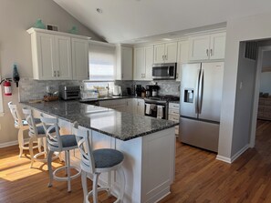 Una cocina moderna con armarios blancos, encimera de granito, electrodomésticos de acero inoxidable y una zona de bar con taburetes blancos.