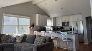 Une cuisine moderne avec des meubles blancs, un réfrigérateur en acier inoxydable et un four à micro-ondes. On y trouve un coin repas avec des chaises blanches et un tabouret de bar.