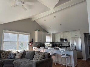 Una cocina moderna con armarios blancos, un refrigerador de acero inoxidable y un microondas. Hay una zona de comedor con sillas blancas y un taburete de bar.