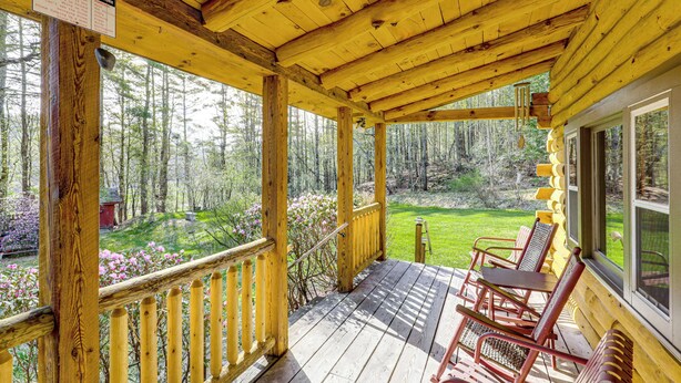 Terraza de madera con un letrero de estación meteorológica, vistas al bosque y mobiliario exterior.