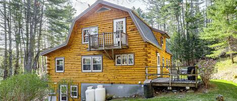A log cabin with a balcony, a deck, and a small garden area.