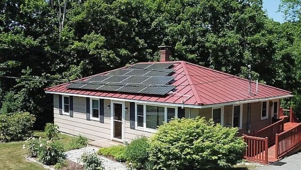 Una casa de un piso con tejado rojo y paneles solares.