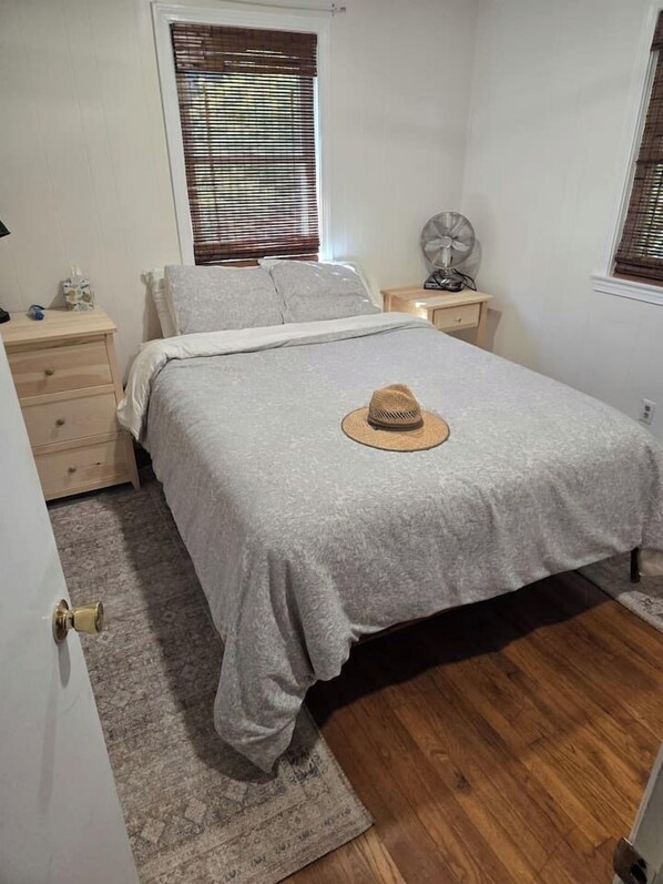 Une chambre à coucher avec un lit, une table de chevet, un ventilateur et une fenêtre avec des stores.