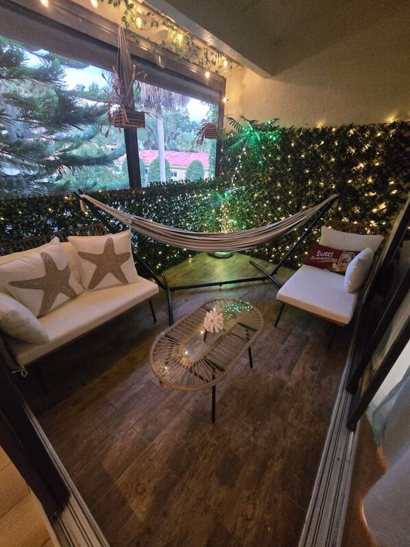 A cozy seating area with a hammock, cushioned chairs, and a glass coffee table.