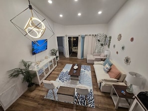 A modern living room with a flat-screen TV, a geometric light fixture, a sofa, a coffee table, and a patterned rug.