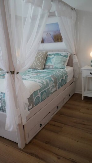 A bed with a canopy, a nightstand, and a painting on the wall.