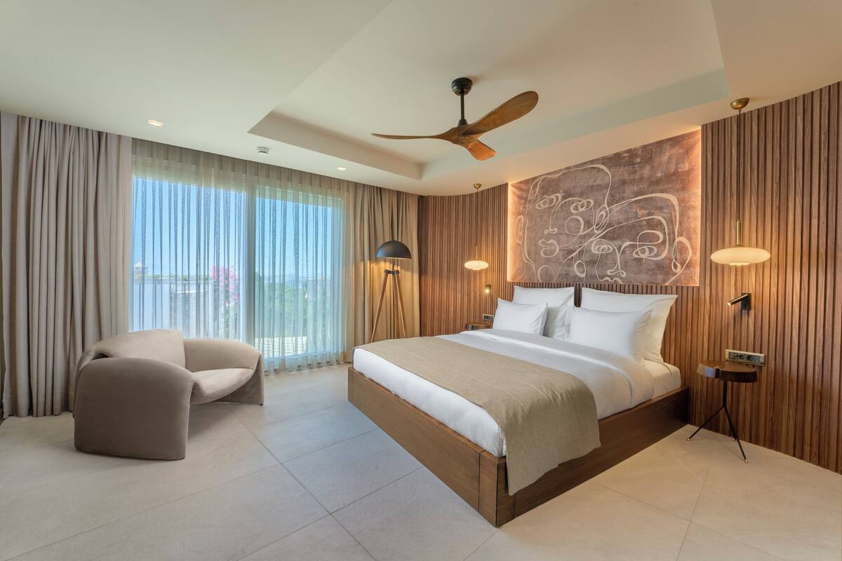 A modern hotel room with a large bed, a chair, and a ceiling fan.