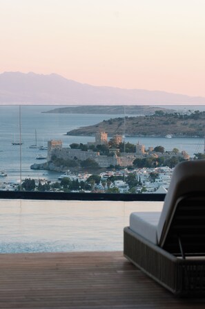 A view of a coastal town with historic buildings and a castle, viewed from a balcony with a wooden floor and a chair. - Mavilu Luxury Hotel (Bodrum)