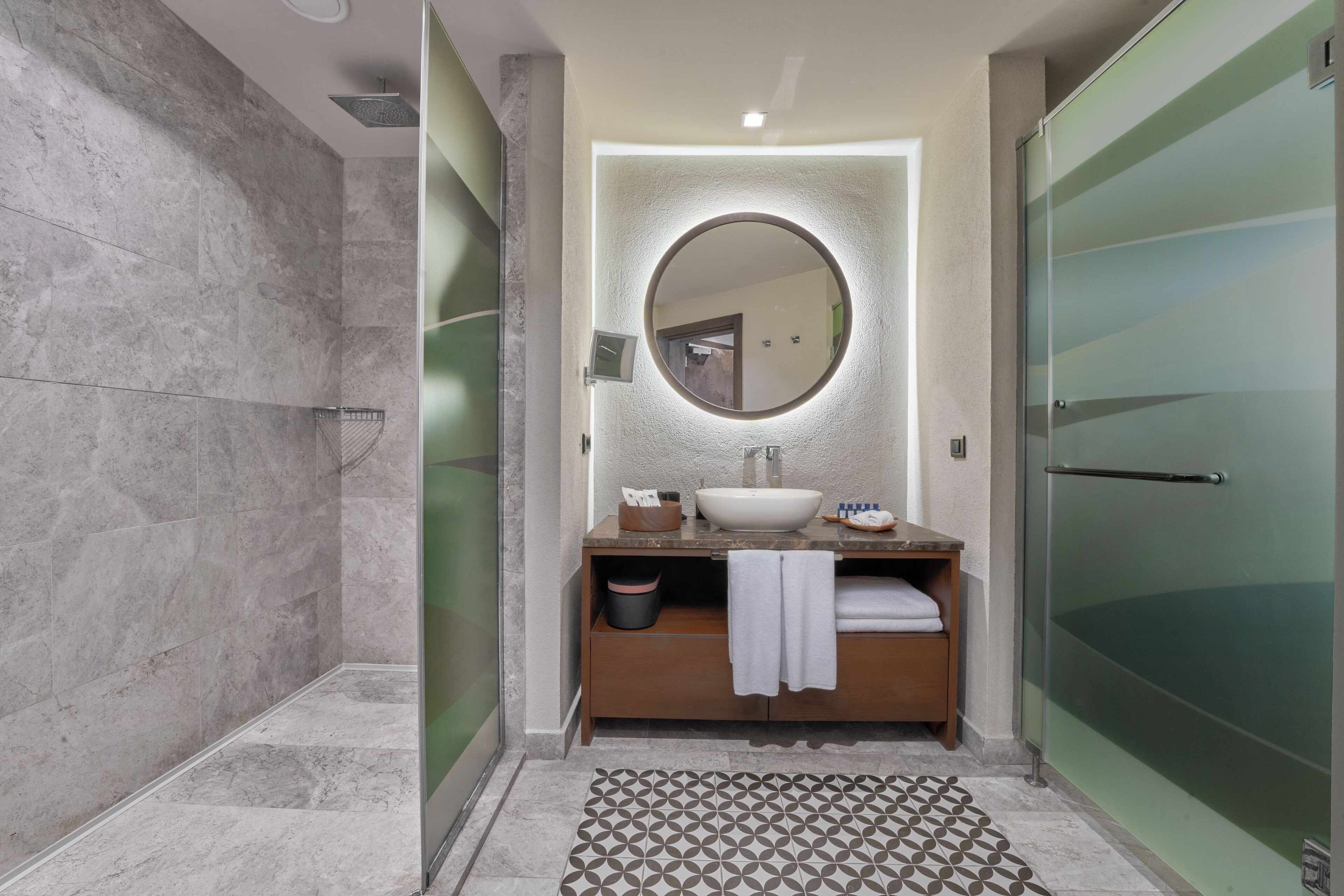 A modern bathroom with a marble shower, a round mirror, a sink, and a glass-enclosed shower stall.