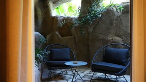 Een klein, afgesloten terras met twee rieten stoelen en een ronde tafel, omringd door natuurstenen muren en groen.