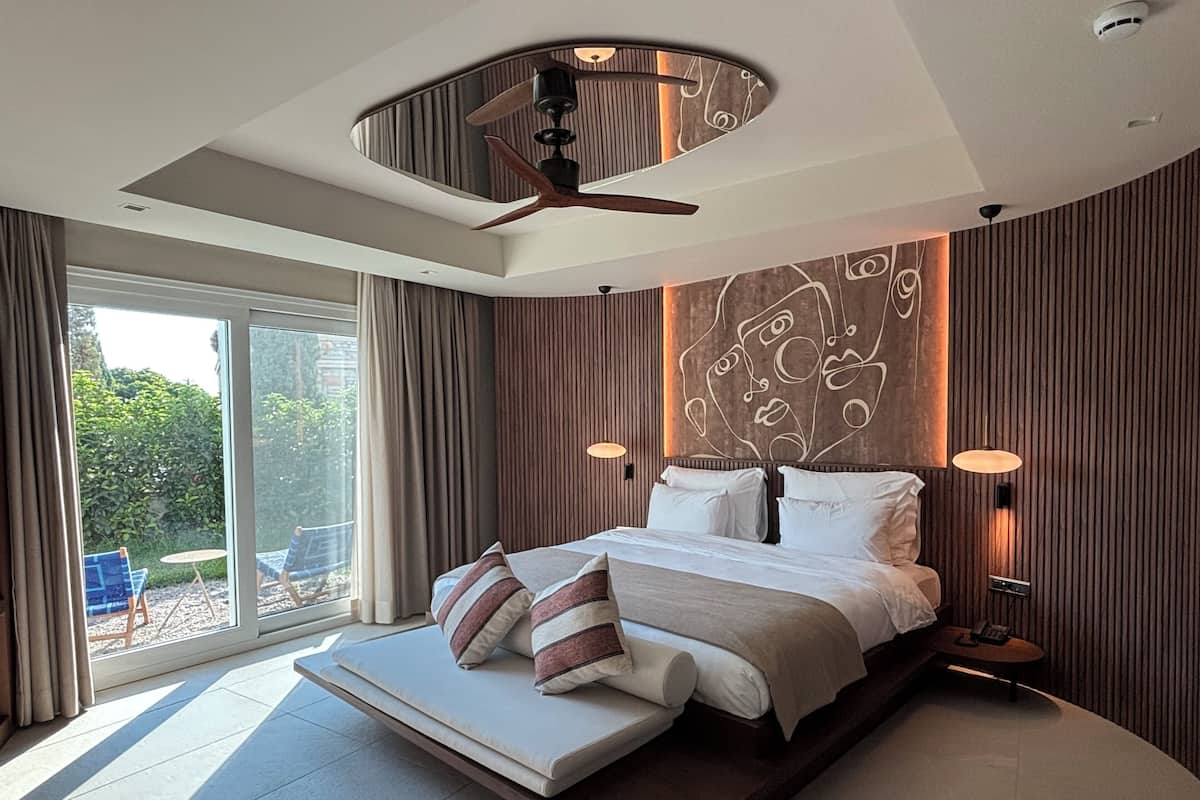 A modern bedroom with a large bed, a ceiling fan, and a view of the outdoors.