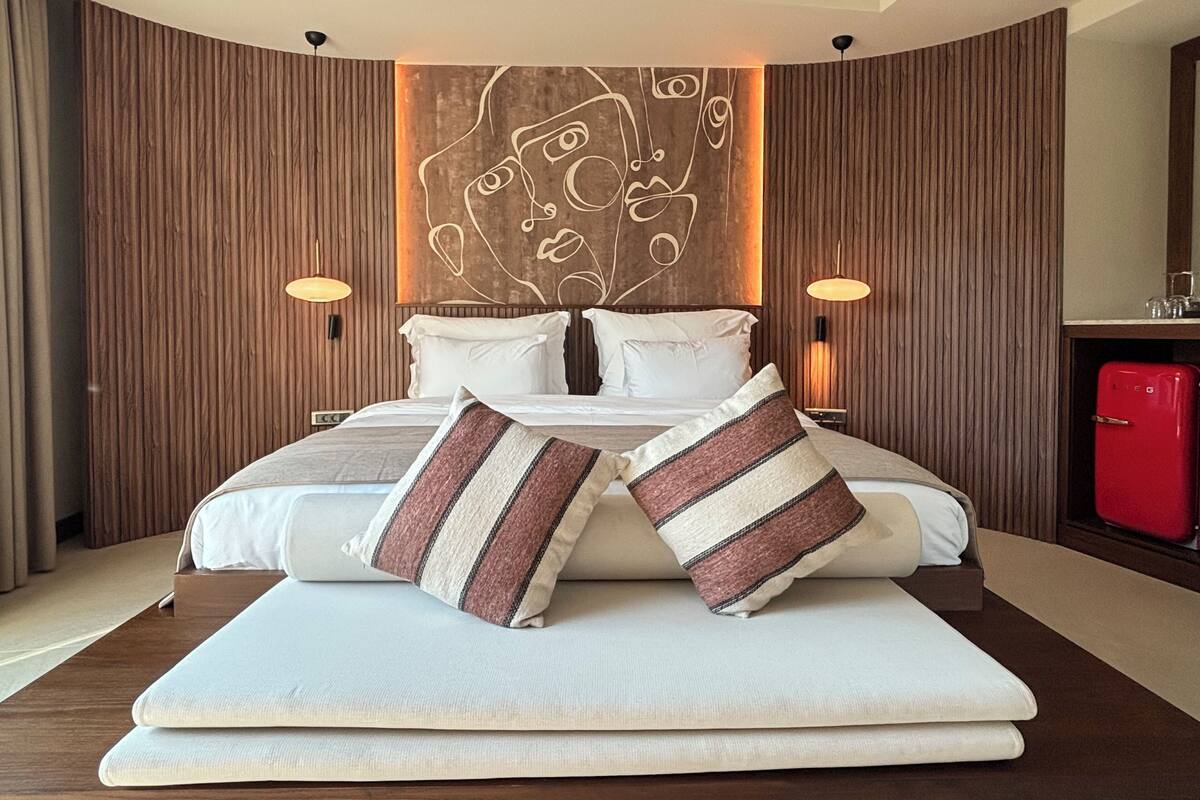 A modern hotel room with a large bed, two bedside lamps, a wooden accent wall, and a red minibar.