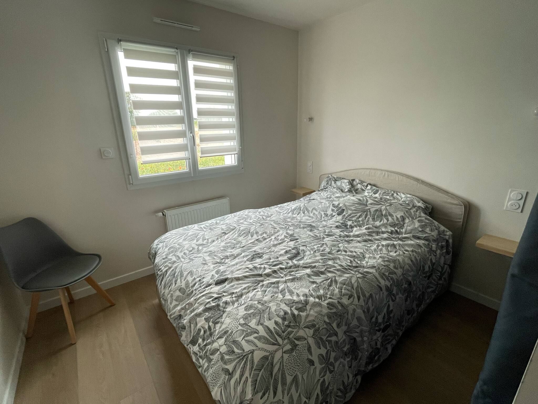 A bedroom with a bed, a chair, a radiator, and a window with blinds.