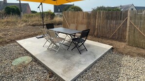 An outdoor patio with a table and chairs, a yellow umbrella, and a wooden fence.