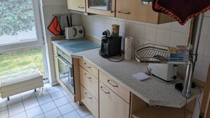 A small kitchen with wooden cabinets, a countertop, a toaster, a kettle, and a window overlooking a garden.