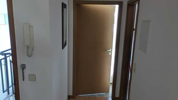A hallway with wooden flooring, a door at the end, and a phone on the wall.