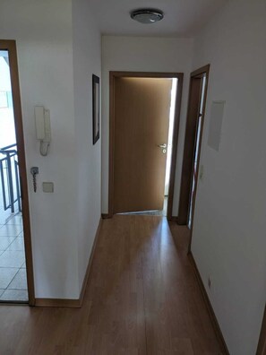 A hallway with wooden flooring, a door at the end, and a phone on the wall. - Vacation apartment (Merseburg)