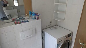 A small laundry room with a washing machine, a drying rack, and various cleaning supplies on the counter.