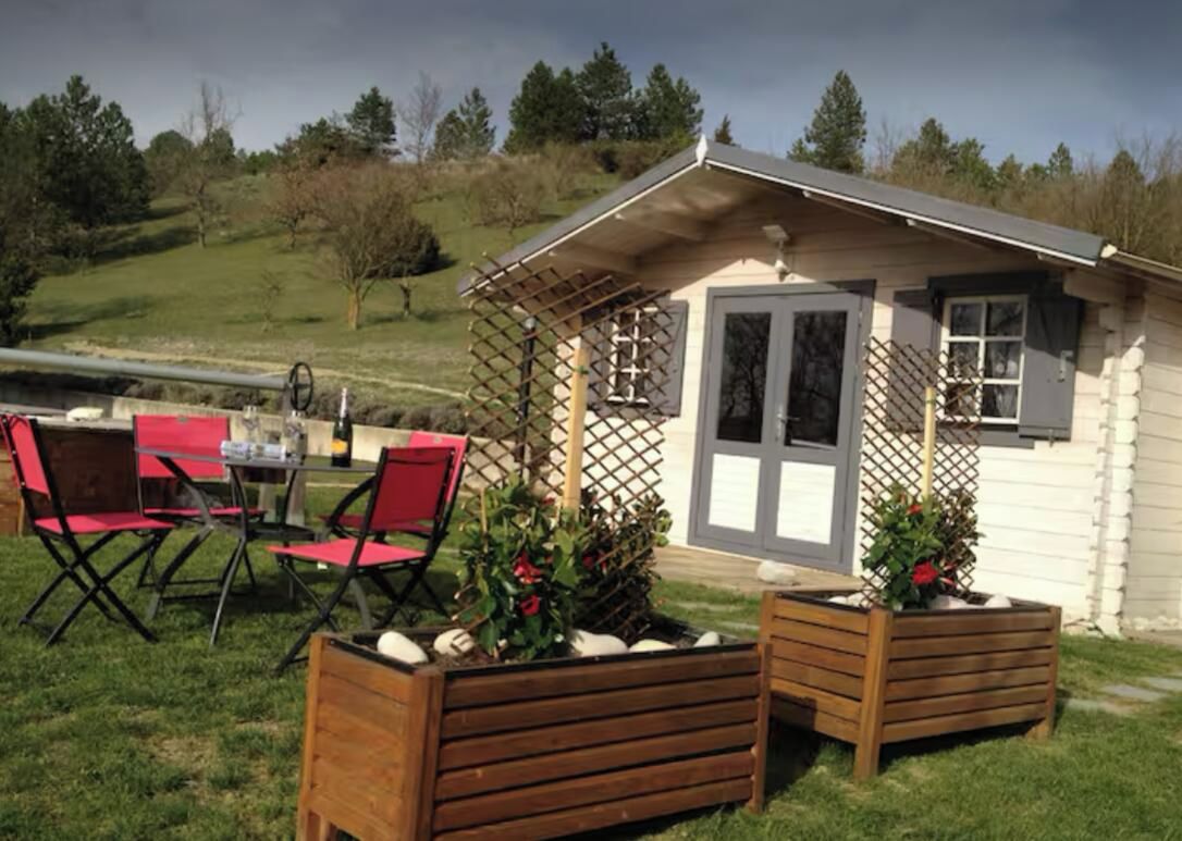 Une petite cabane en bois avec une véranda, des chaises rouges et des plantes en pot.