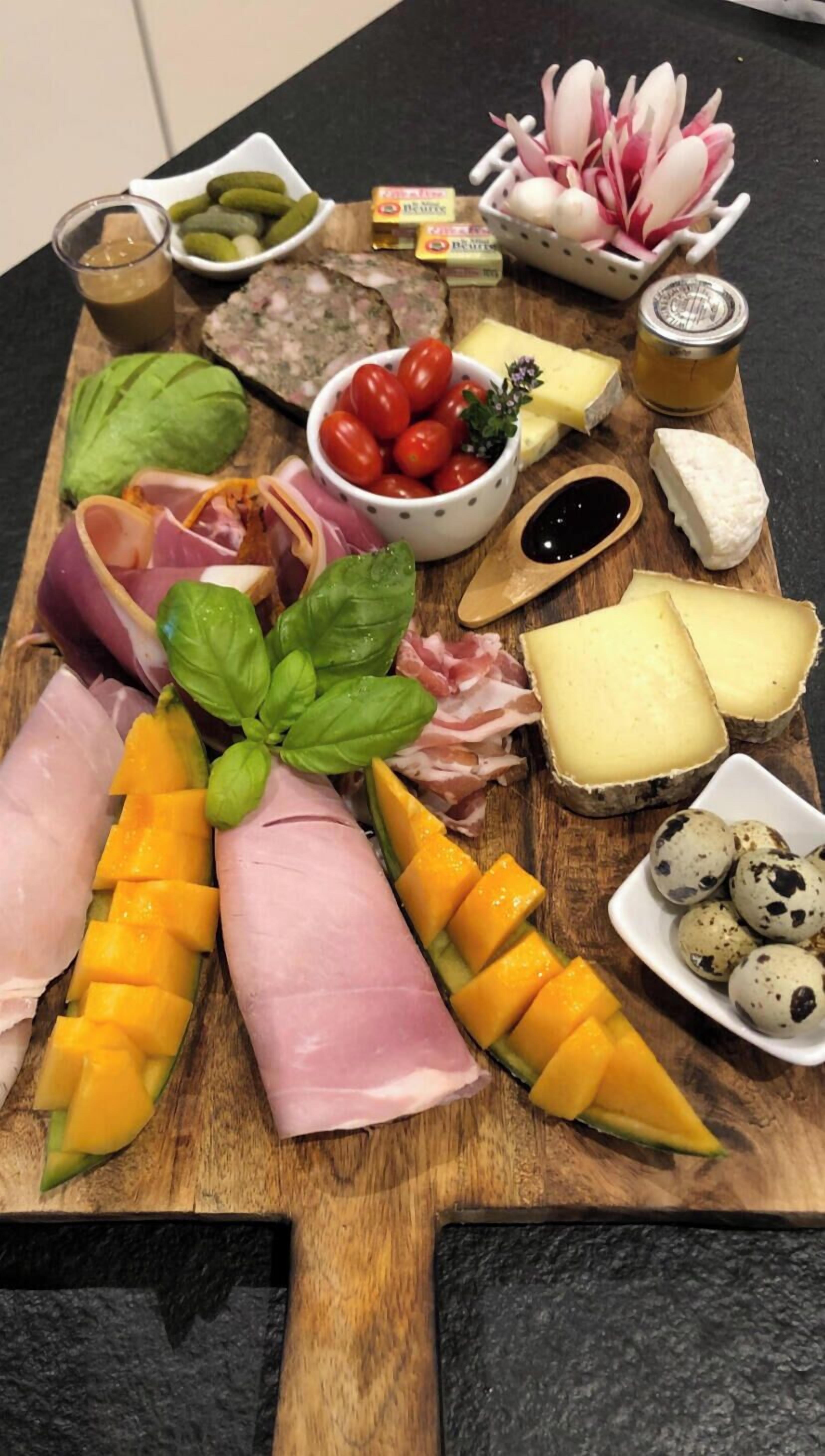 A wooden board with various food items including meats, cheese, and fruits.