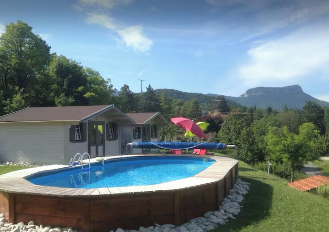 A backyard with a swimming pool, a wooden deck, and a mountain in the background.
