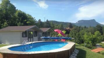 A backyard with a swimming pool, a wooden deck, and a mountain in the background.
