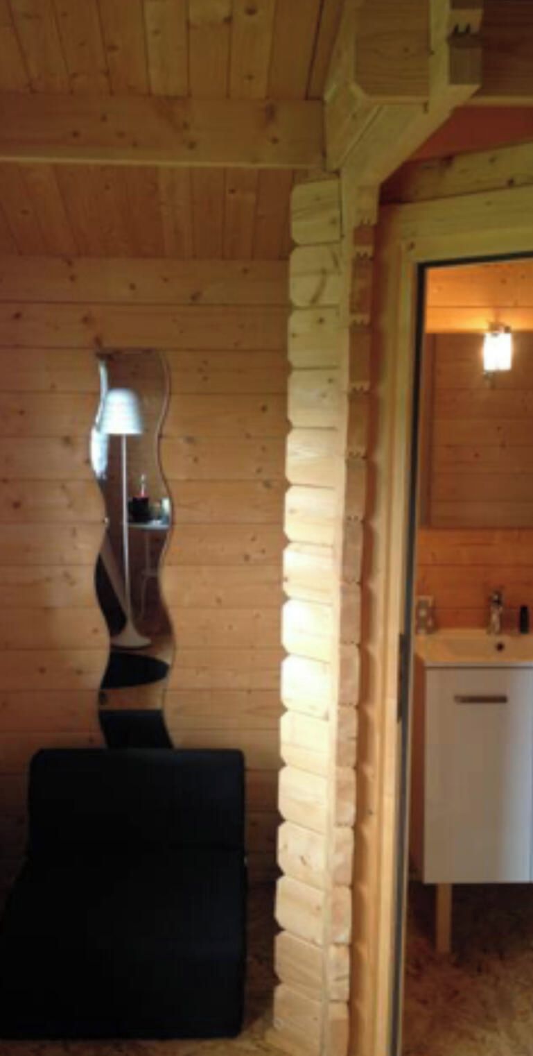 Interno di una baita in legno con parete in pietra, un poggiapiedi nero e un armadietto bianco.