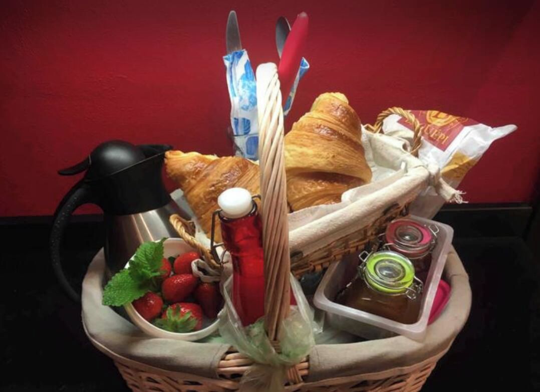 A basket containing croissants, strawberries, a red bottle, and a thermos.