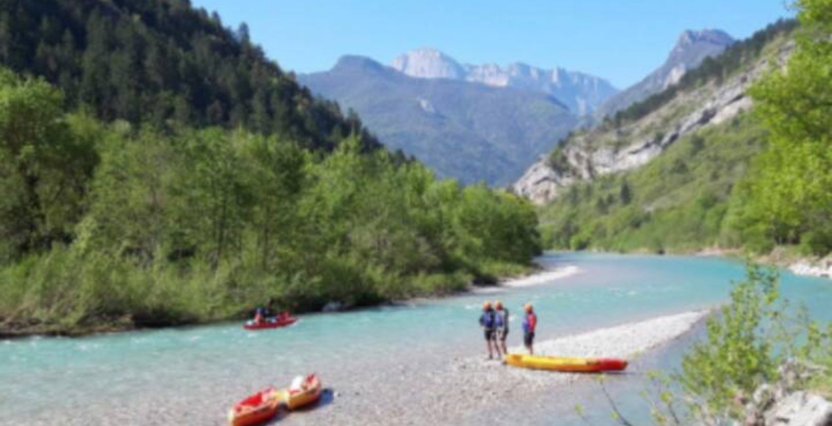 A river with kayaks and a group of people near the shore.