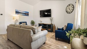 Un salon avec un canapé, un fauteuil, une télévision et une horloge au mur.