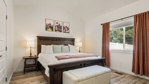 Une chambre à coucher avec un lit en bois, deux tables de chevet avec des lampes, un banc et une fenêtre avec des rideaux.