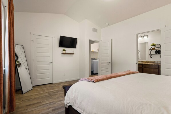 A bedroom with a bed, a TV, a mirror, and a door leading to a bathroom.