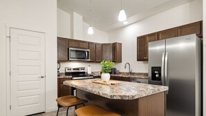 Une cuisine moderne dotée d’un îlot central, d’appareils électroménagers en acier inoxydable et de meubles de rangement en bois.