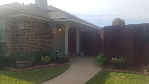 A residential house with a brick exterior, a number '703' sign, an American flag, and a wooden fence. - Long-term in Grapevine close to everything (Grapevine)