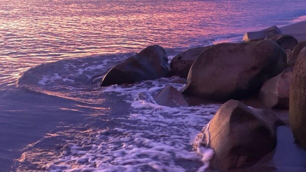 Une plage avec de gros rochers et des vagues au coucher du soleil.